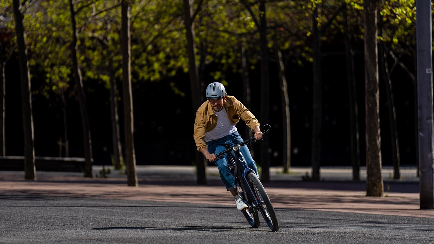 A person in a beige jacket and helmet rides a Stromer ST7 Alinghi Red Bull Racing Edition eBike on an urban street, maneuvering sharply around a corner.