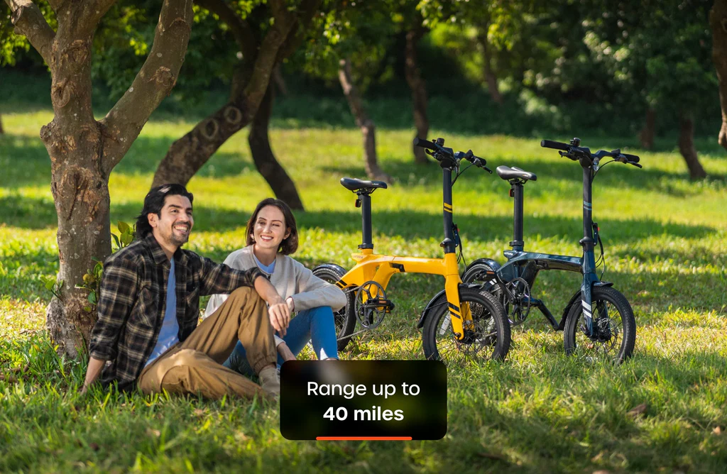 Two people relax on grass under trees beside two Urtopia Carbon Fold 1 eBikes, featuring a high-torque motor; a display overlay reads "Range up to 40 miles.