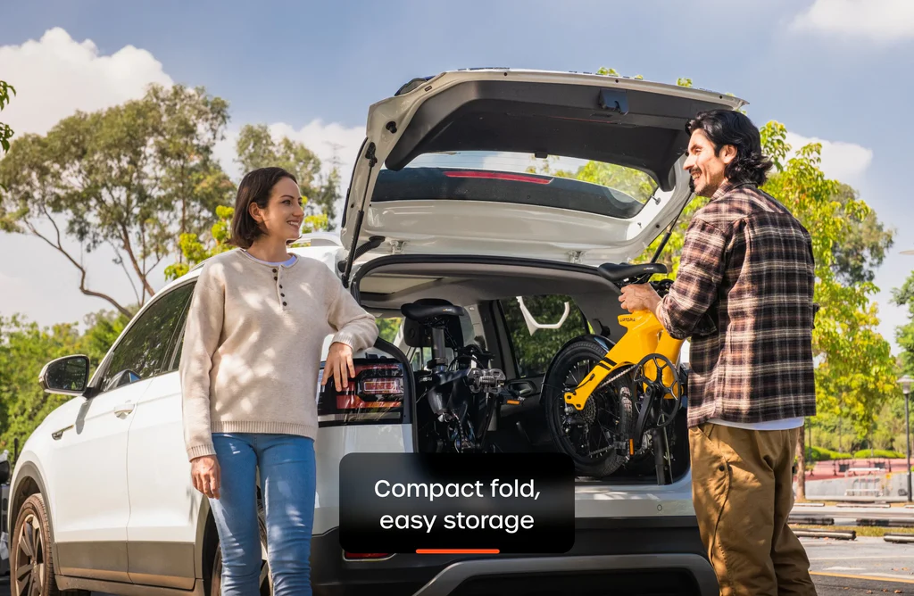 Two people load a yellow Urtopia Carbon Fold 1 eBike into an SUV trunk. Text overlay: "Compact fold, easy storage.