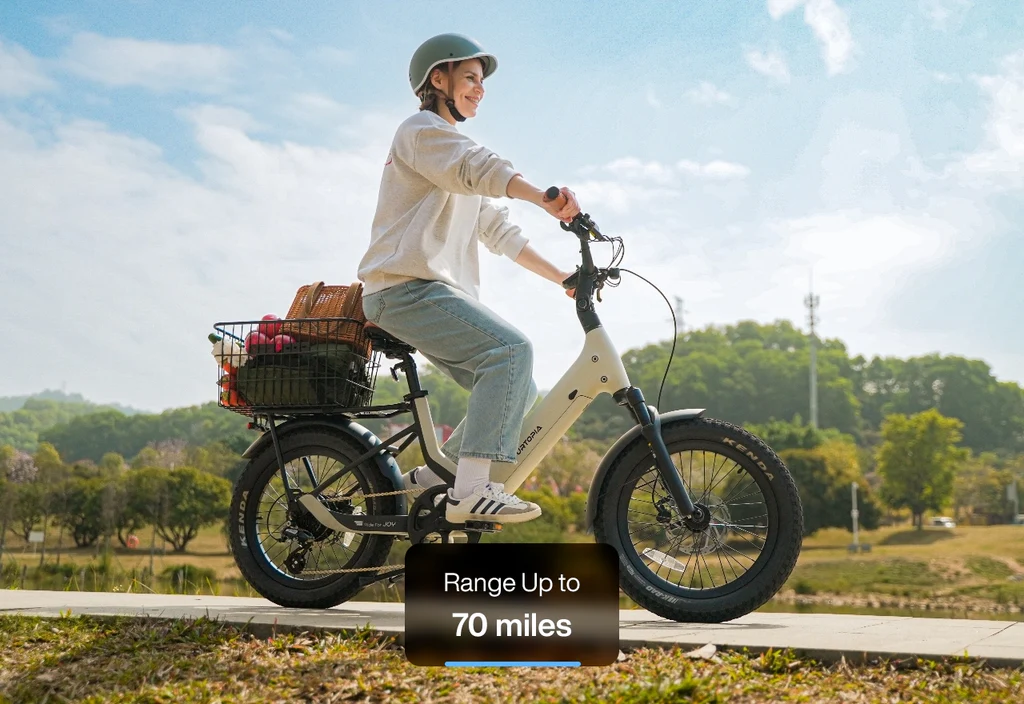 A rider in a helmet cruises on the Urtopia - Joy Carbon eBike by Urtopia, featuring a carbon frame and a grocery basket; overlay text: "Range Up to 70 miles.