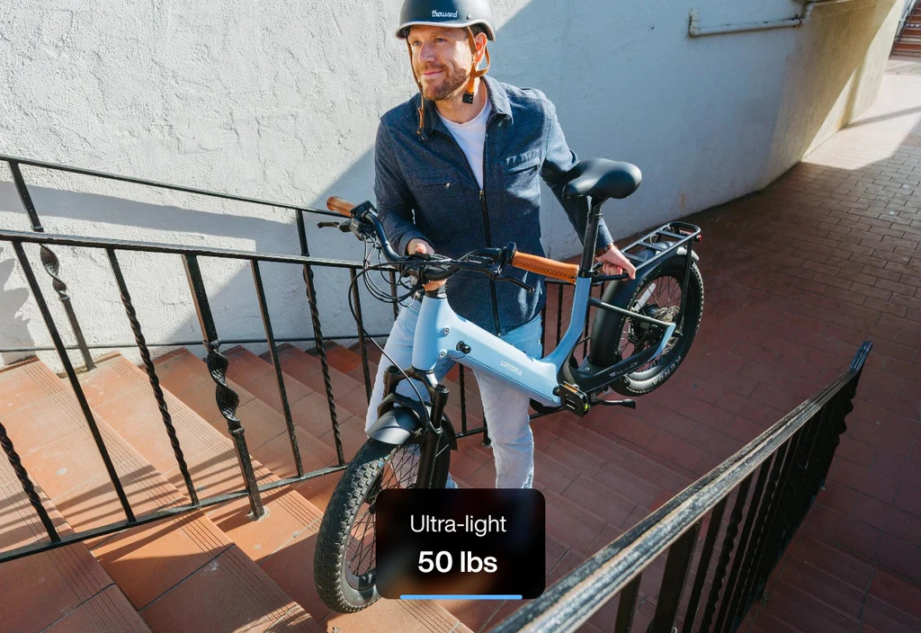 A man in a helmet carries a light blue Urtopia - Joy Carbon eBike with a carbon frame up stairs. A label on the image reads "Ultra-light 50 lbs.