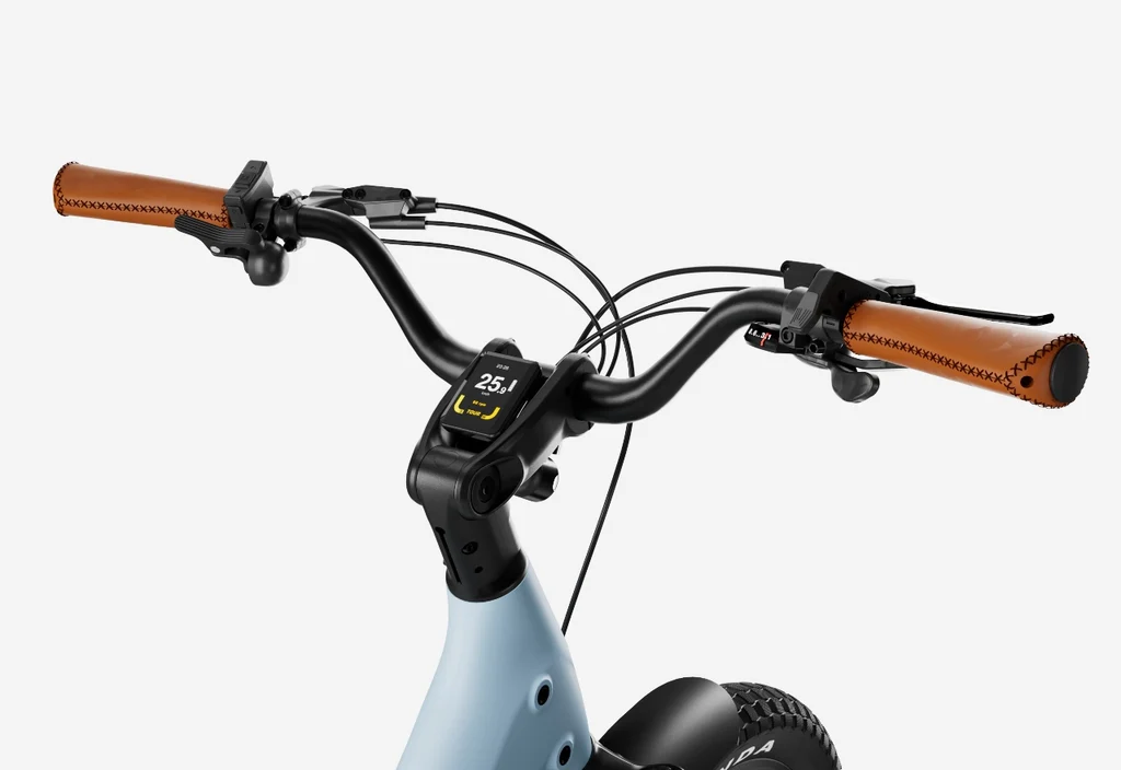 Close-up of Urtopia - Joy Carbon eBike handlebars with brown grips, a digital display reading 25.1 km/h, and multiple control cables set against a plain background.