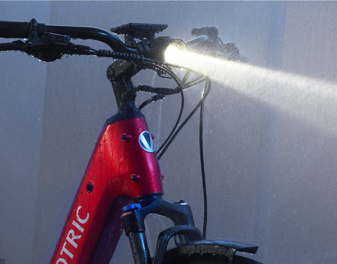 Close-up of a red Velotric - Discover 1 in the rain, with its headlight on, showcasing the sleek design from Tampa Bay eBikes.