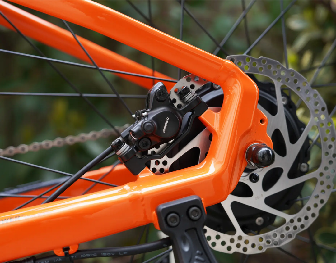 Close-up of the rear brake system and sprocket on an orange Velotric Summit 1 eBike, showing detailed view of the disc brake and chain.