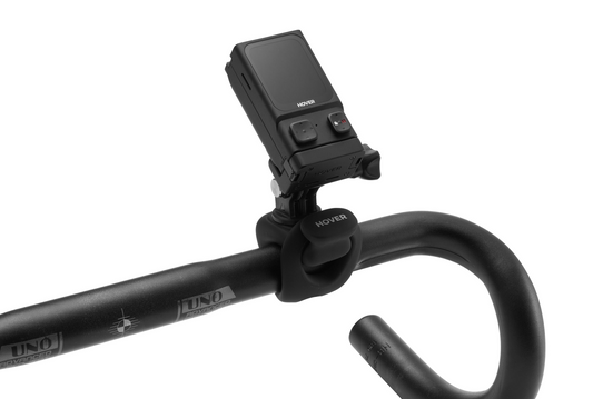 A black camera, reminiscent of the innovative HoverAir X1, is attached to a curved bike handlebar using a HOVERAir HandleBar Mount by HOVERAir.