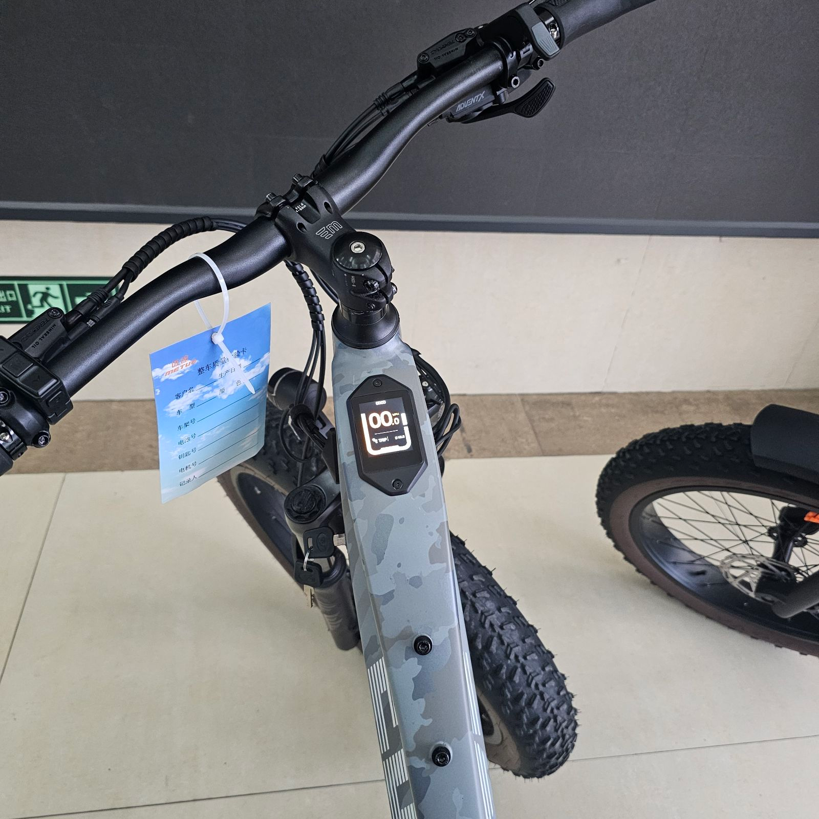 Close-up of the Magnum - Edge by Tampa Bay eBikes: handlebars and display screen showing 100% battery, with a tag hanging from the brake lever.