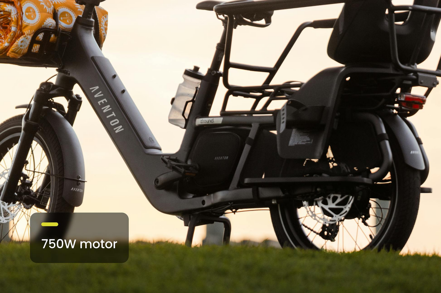 Outdoor sunset side view of the Aventon - Abound LR cargo e-bike by Aventon, featuring a 750W motor, rear rack, and cargo bag.