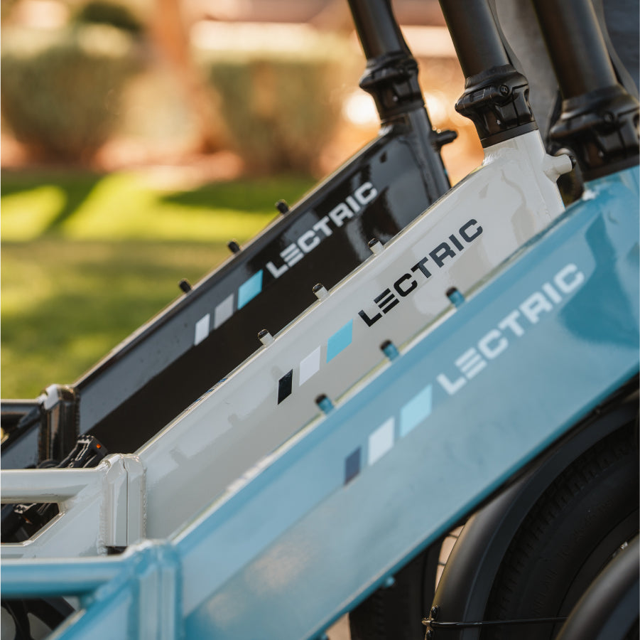 Close-up of three Lectric XP4 folding eBike frames—black, white, and blue—lined up outdoors, each featuring a powerful 750W rear hub motor.