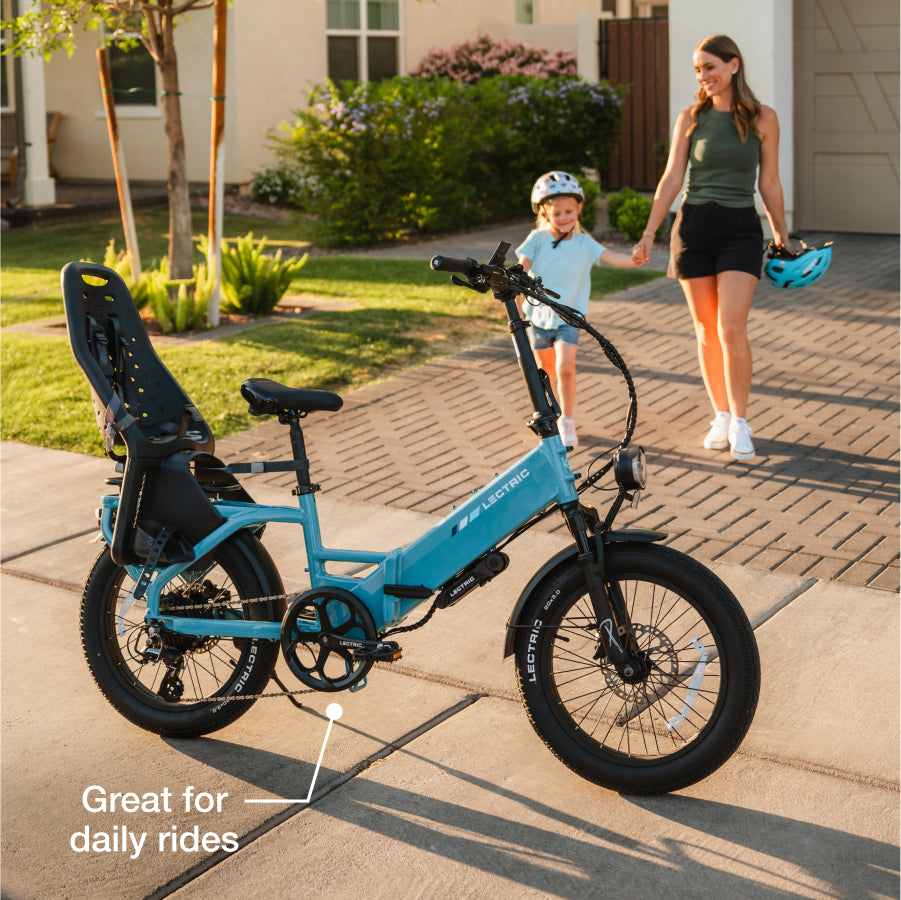 A blue Lectric XP4 e-bike with a child seat is parked on a driveway as a woman and child walk by. Text: "Great for daily rides." Get your Lectric XP4 at Tampa Bay eBikes.
