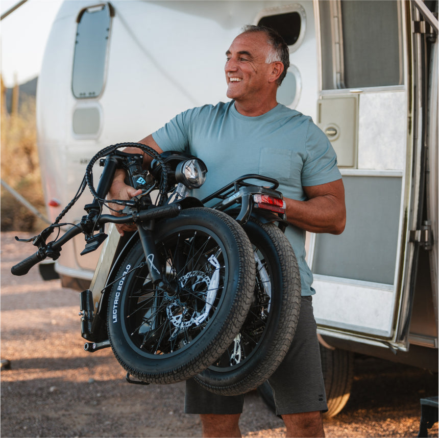 A man stands outside an RV, smiling as he holds a folded Lectric XP4 eBike from Lectric, ready for his next adventure.