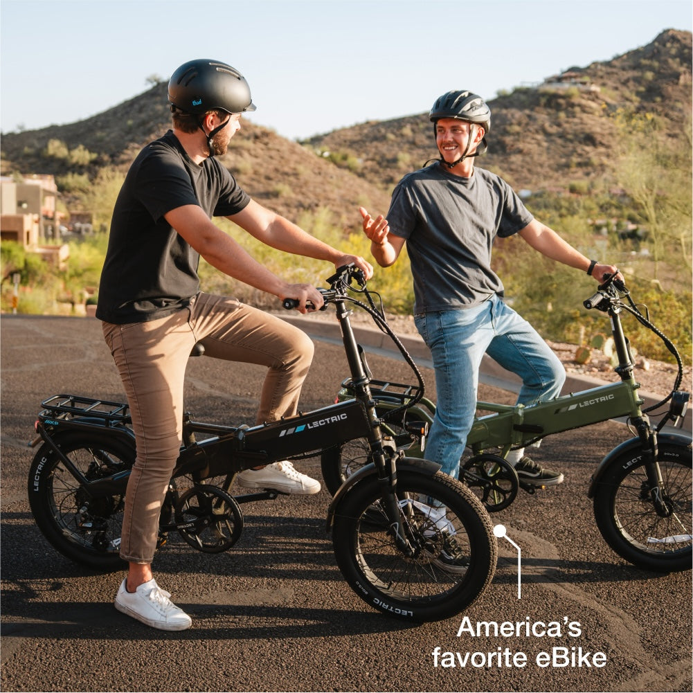 Two men wearing helmets sit on Lectric XP4 folding eBikes with 750W rear hub motors, smiling and talking on a paved road with hills and houses in the background. Text reads, "America’s favorite eBike.