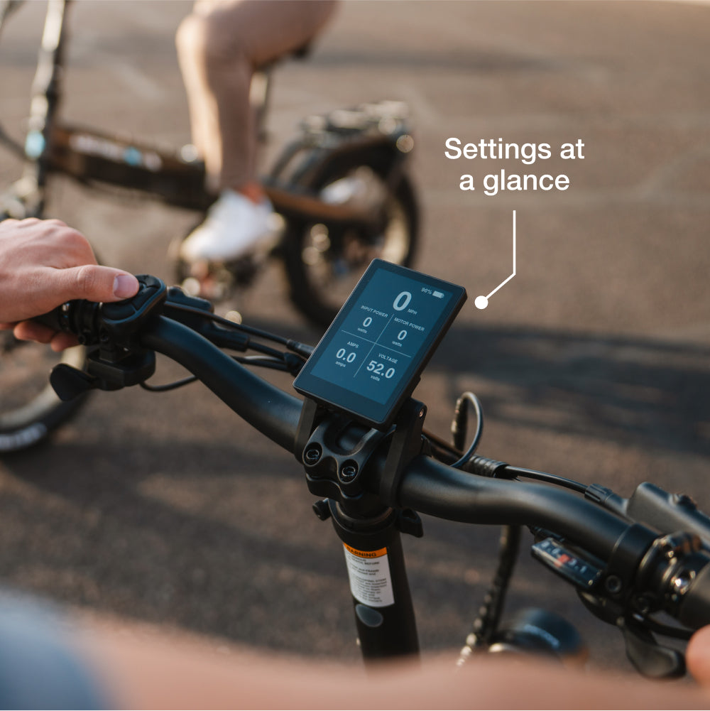 Close-up of a Lectric XP4 handlebar display with "Settings at a glance" highlighted; in the background, another rider travels the trail on the folding Lectric eBike featuring advanced torque sensor technology.