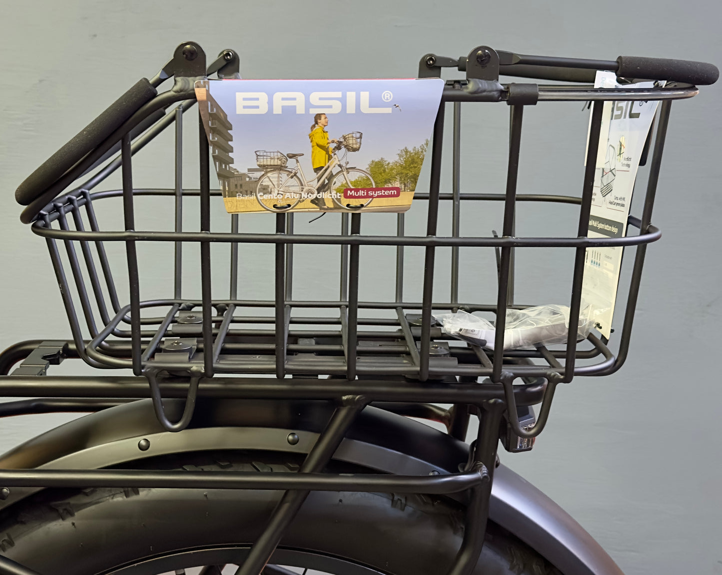 A black metal Basil Cento MIK rear basket is mounted on the bike’s MIK system, featuring attached tags and visible product details.