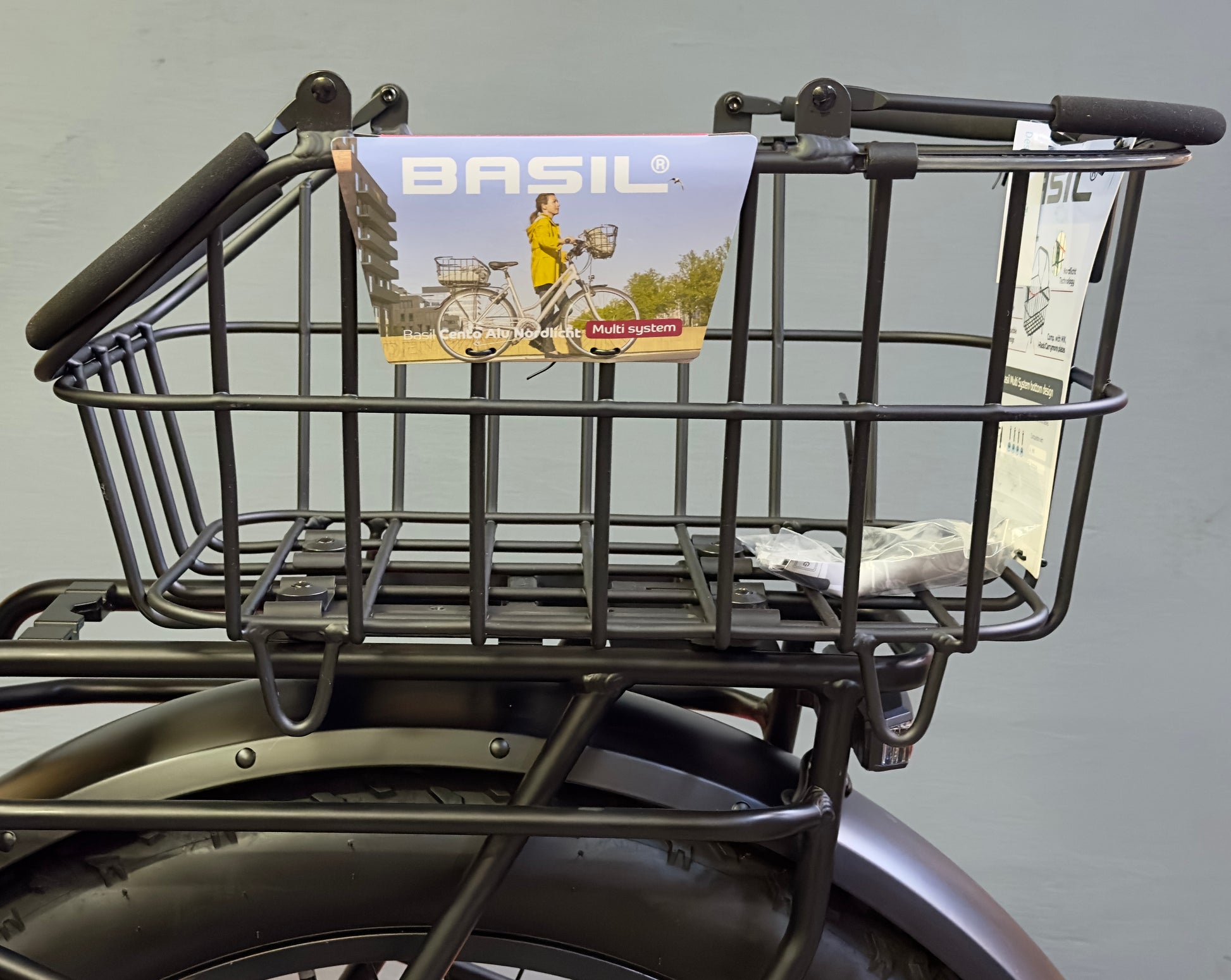 A black metal Basil Cento MIK rear basket is mounted on the bike’s MIK system, featuring attached tags and visible product details.
