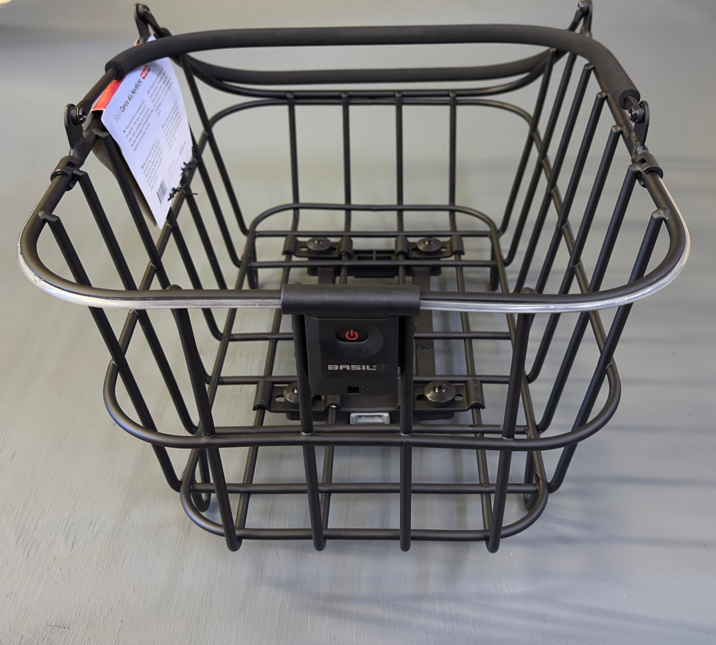 The Basil Cento MIK rear basket in black, complete with mounting hardware and label, is shown on a light gray surface.