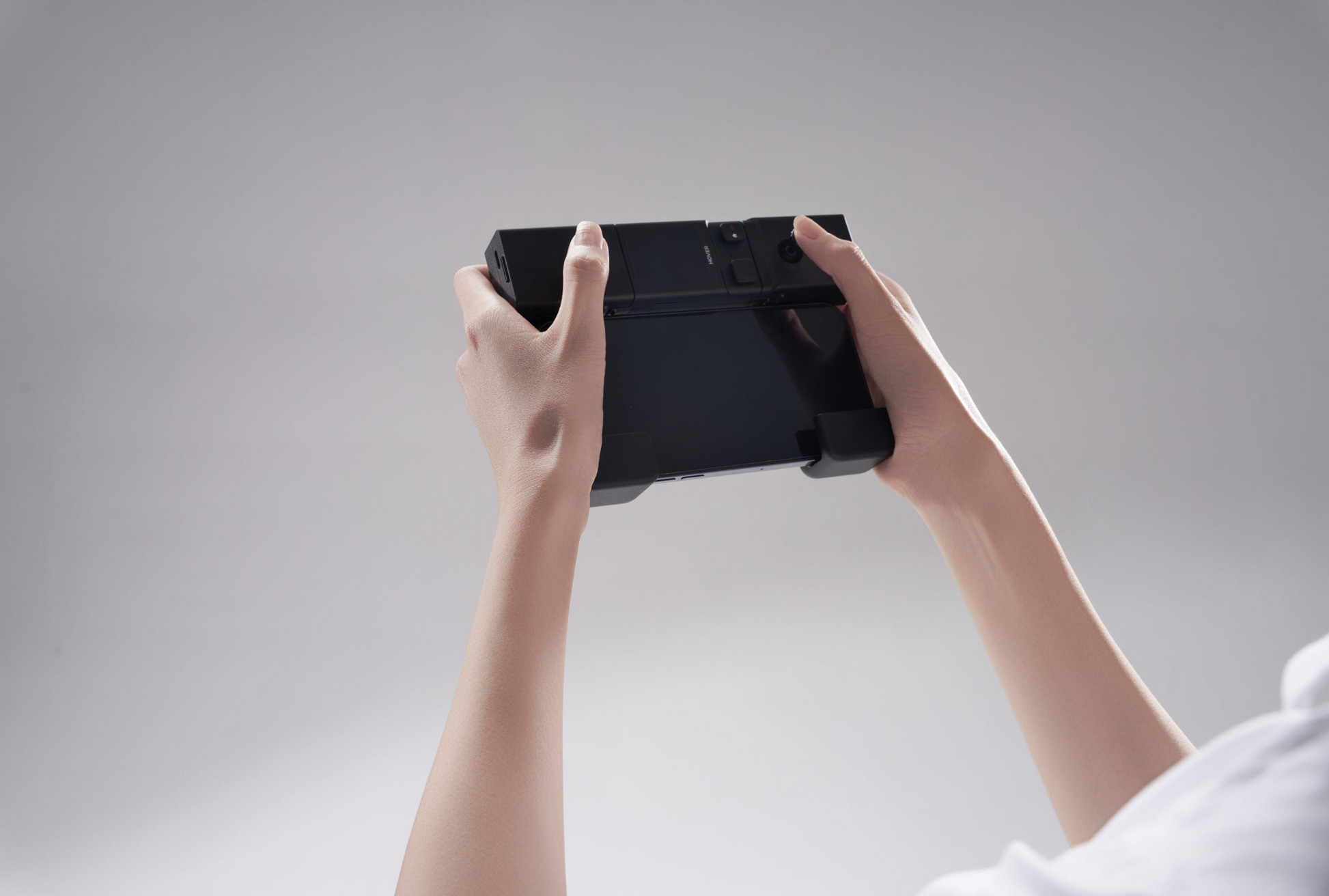 Hands holding the HOVERAir Beacon and JoyStick Bundle, a portable gaming console by HOVERAir, against a plain gray background.