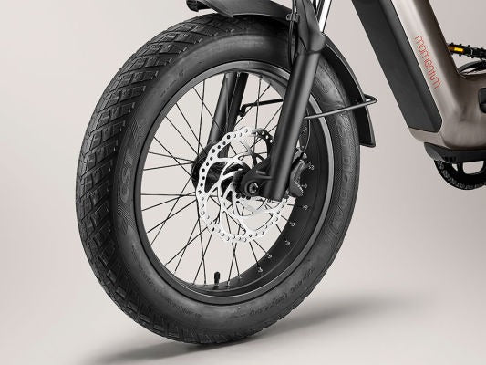 Close-up of a Momentum - Cito E+ front wheel with detailed view of the tire tread, disc brake, and suspension fork on a plain background featuring the Tampa Bay eBikes logo.