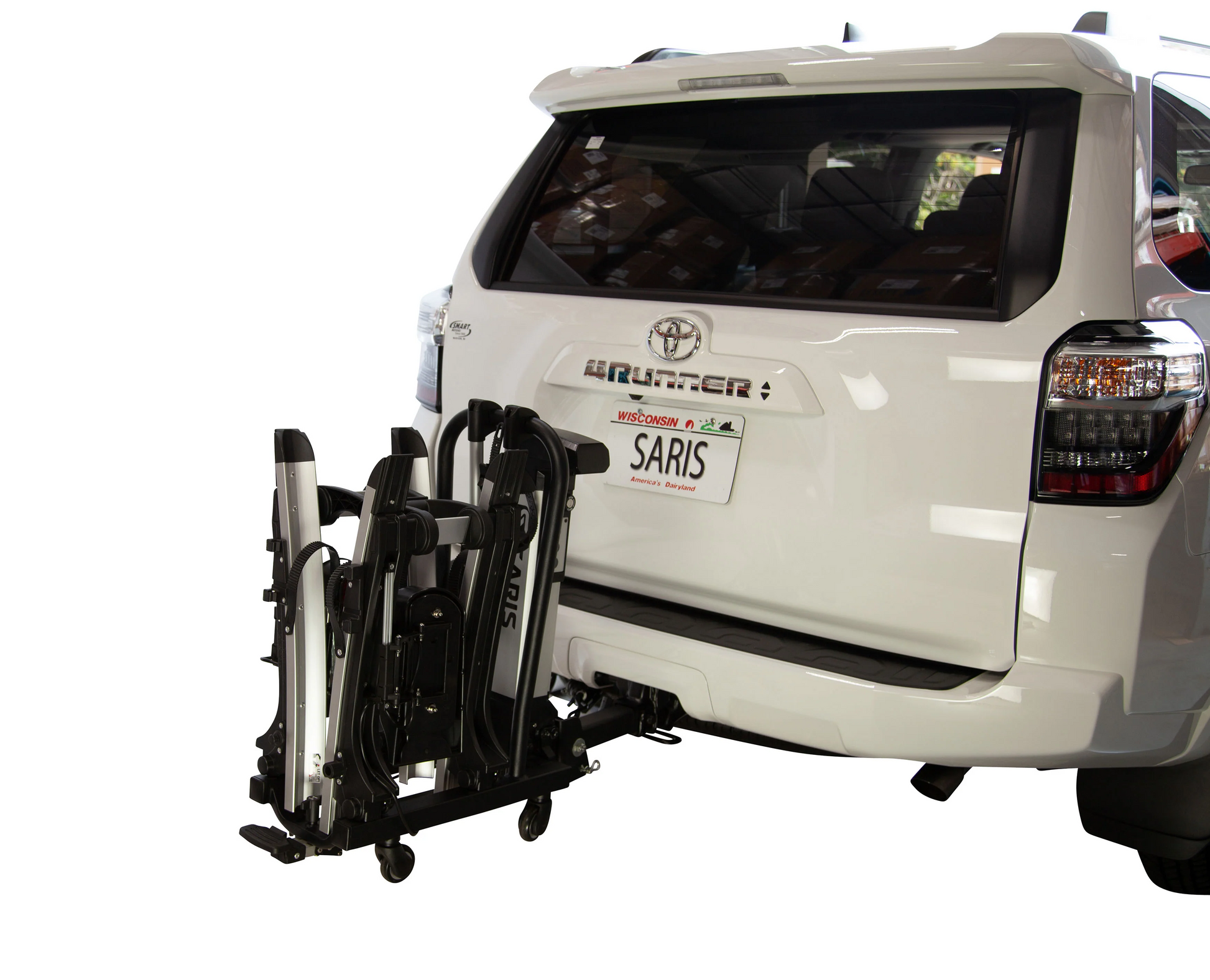 A white SUV with a Saris - Door County 2-Bike Motorized Hitch Rack by Hollywood Racks on the rear hitch is parked in a garage.