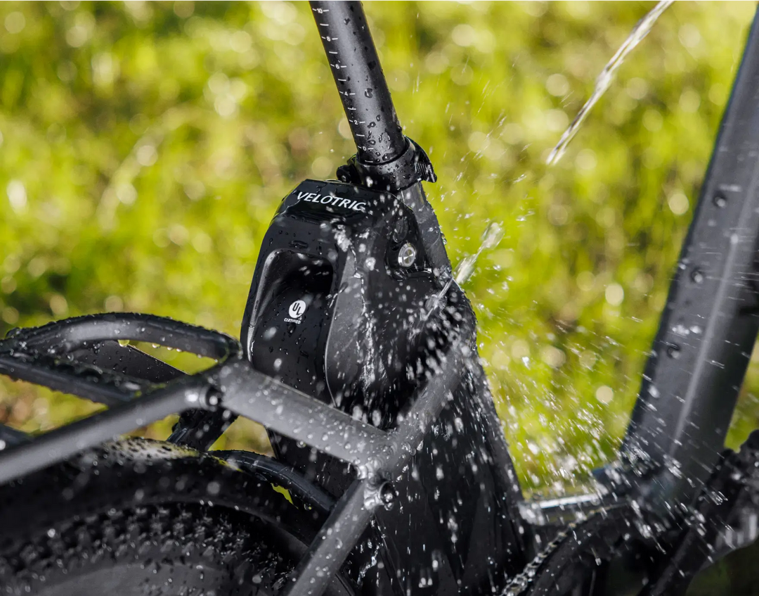 Close-up of a black Velotric Fold 1 eBike frame being splashed with water, highlighting the Velotric logo and water droplets in sharp focus.