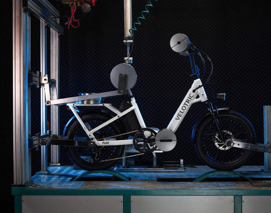 Velotric - Fold 1 electric bicycle undergoing mechanical testing in a laboratory setup, positioned on a metal rig with various sensors attached to assess its long-range battery performance.