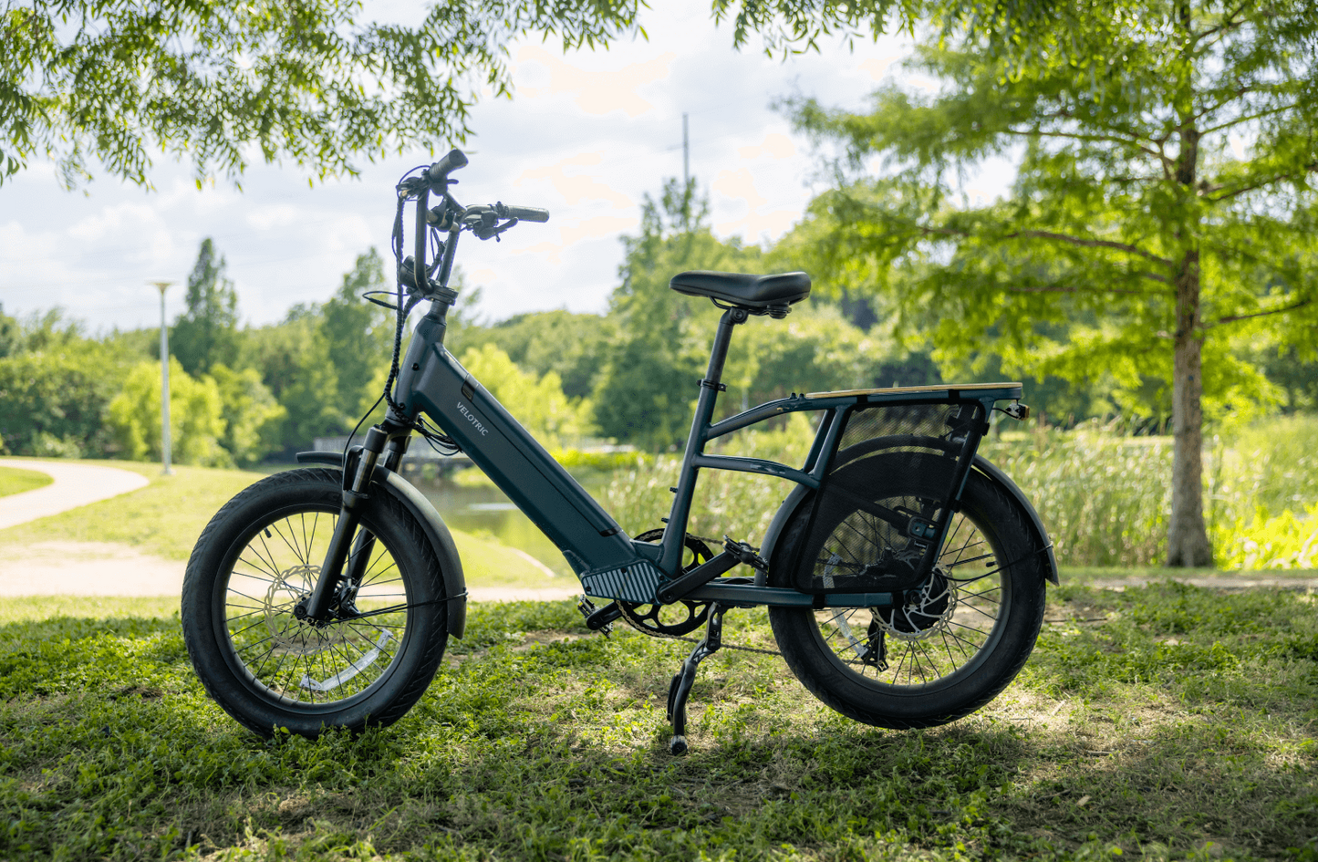 Electric bicycle, specifically a Velotric Go 1 - Forest, parked on grass with trees and a path in the background on a sunny day.