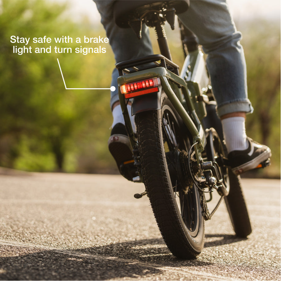 Rear view of a person riding the Lectric XP4 folding eBike from Lectric, featuring brake light and turn signals for safety; text highlights its impressive 85-mile range.