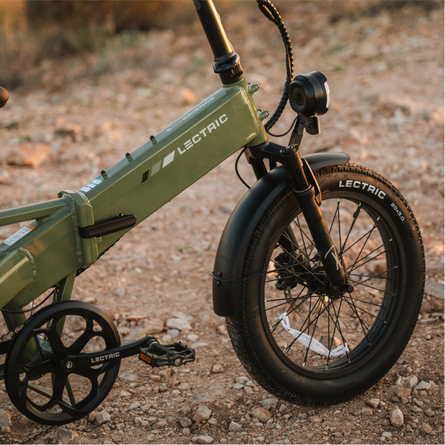 Close-up of the front wheel and frame of a green Lectric XP4 Folding eBike by Lectric on a rocky outdoor path, highlighting its advanced Torque Sensor Technology.
