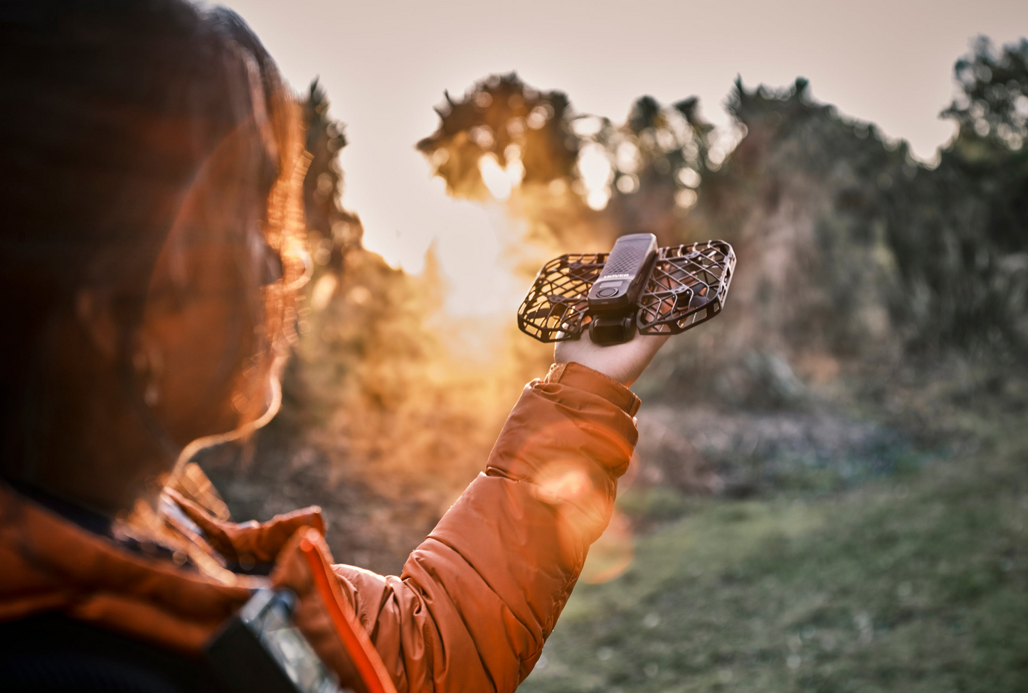 Someone cradles the HOVERAir X1 Pro, an AI-powered drone by HOVERAir, outdoors at sunset as golden sun rays filter through the trees.