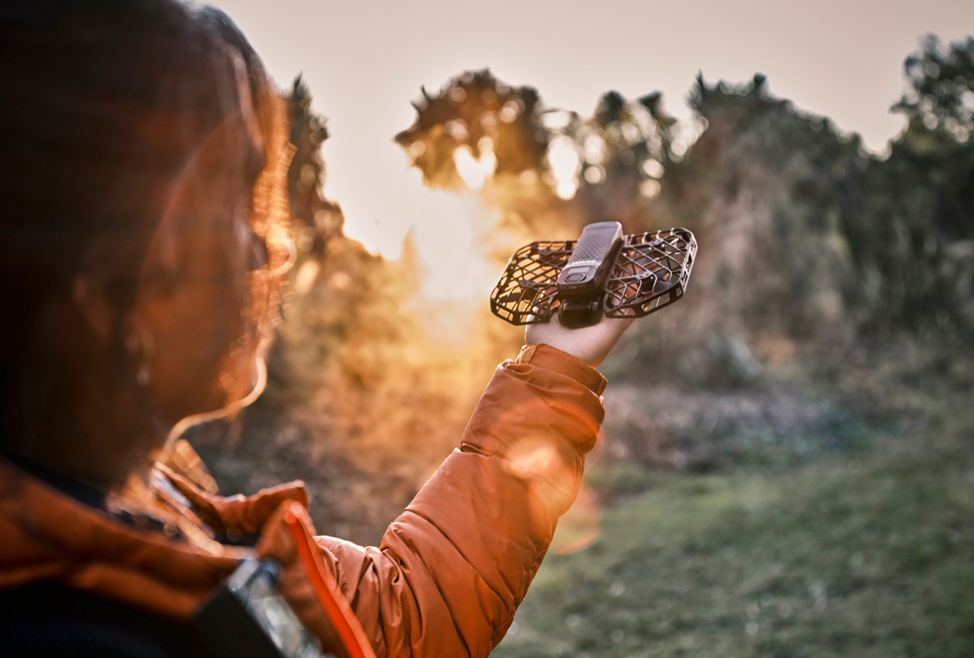 Someone cradles the HOVERAir X1 Pro, an AI-powered drone by HOVERAir, outdoors at sunset as golden sun rays filter through the trees.
