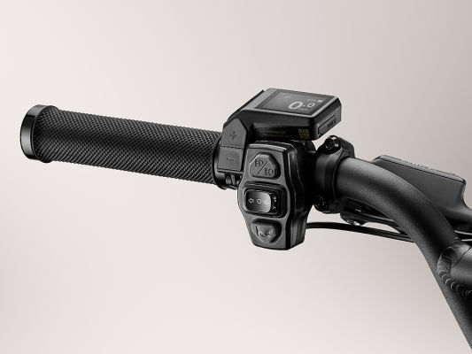 Close-up of a motorcycle handlebar with electronic control switches and a digital display on a light background, featuring Momentum - Cito E+ from Tampa Bay eBikes.