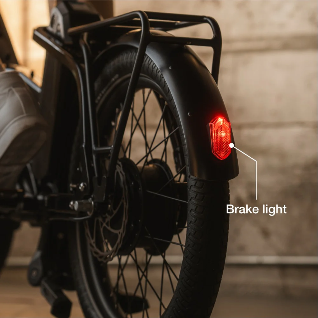 Close-up of the rear wheel of the Lectric - ONE bicycle by Lectric, showing an illuminated red brake light with a pointer highlighting the brake light.