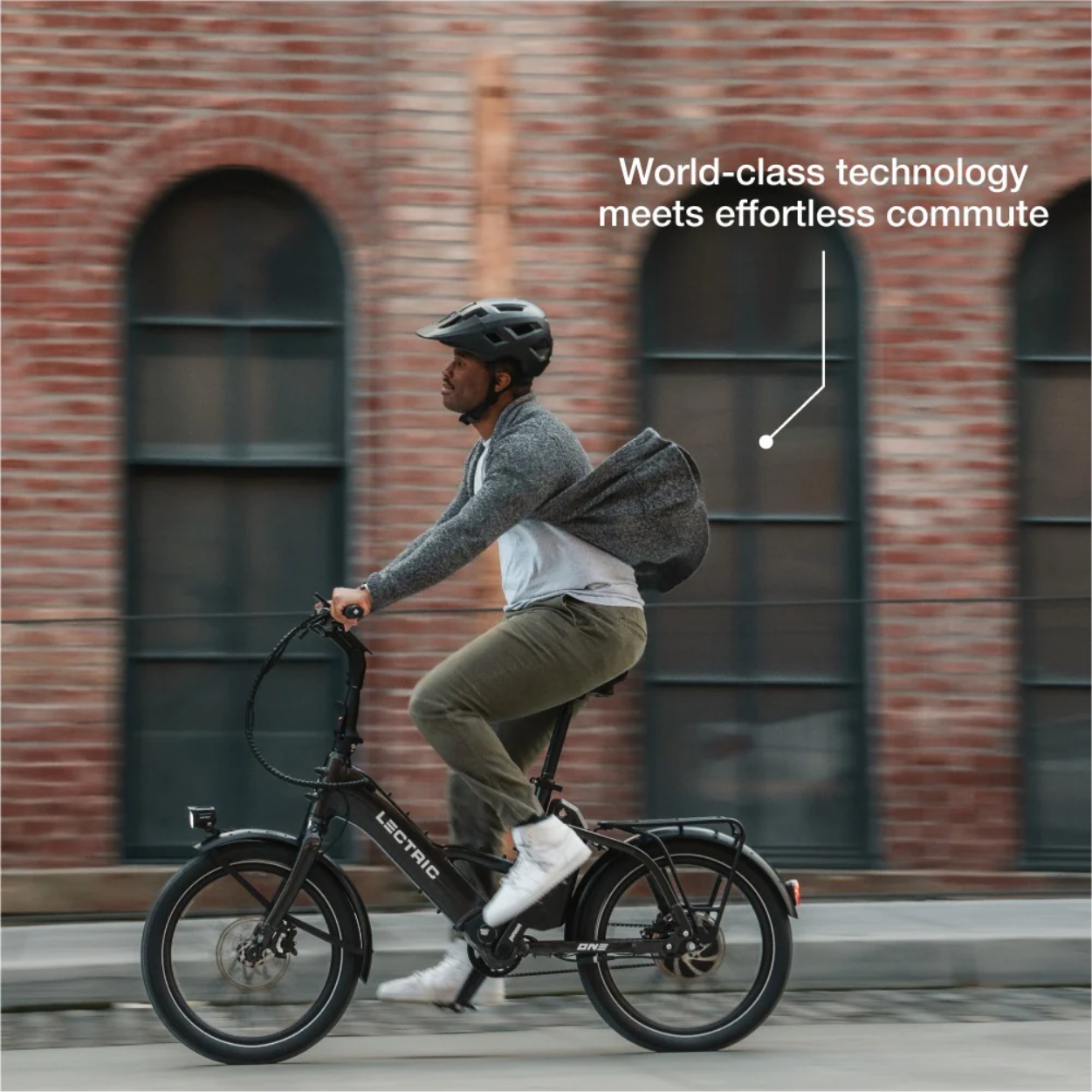A person wearing a helmet rides the Lectric - ONE e-bike past a brick building, with text reading "World-class technology meets effortless commute.