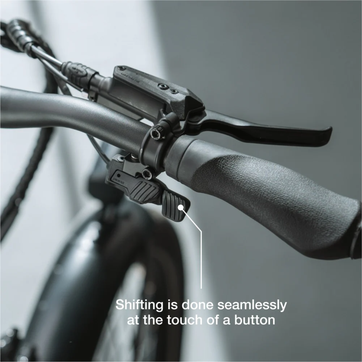 Close-up of the Lectric - ONE handlebar featuring a gear shifter with an easy-to-use button; text reads, "Shifting on the Lectric - ONE is seamless at the touch of a button.