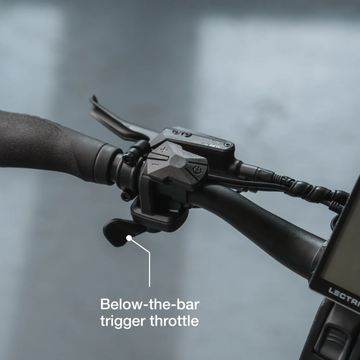 Close-up of the Lectric - ONE bicycle handlebar displaying a below-the-bar trigger throttle, with text labeling the throttle mechanism.