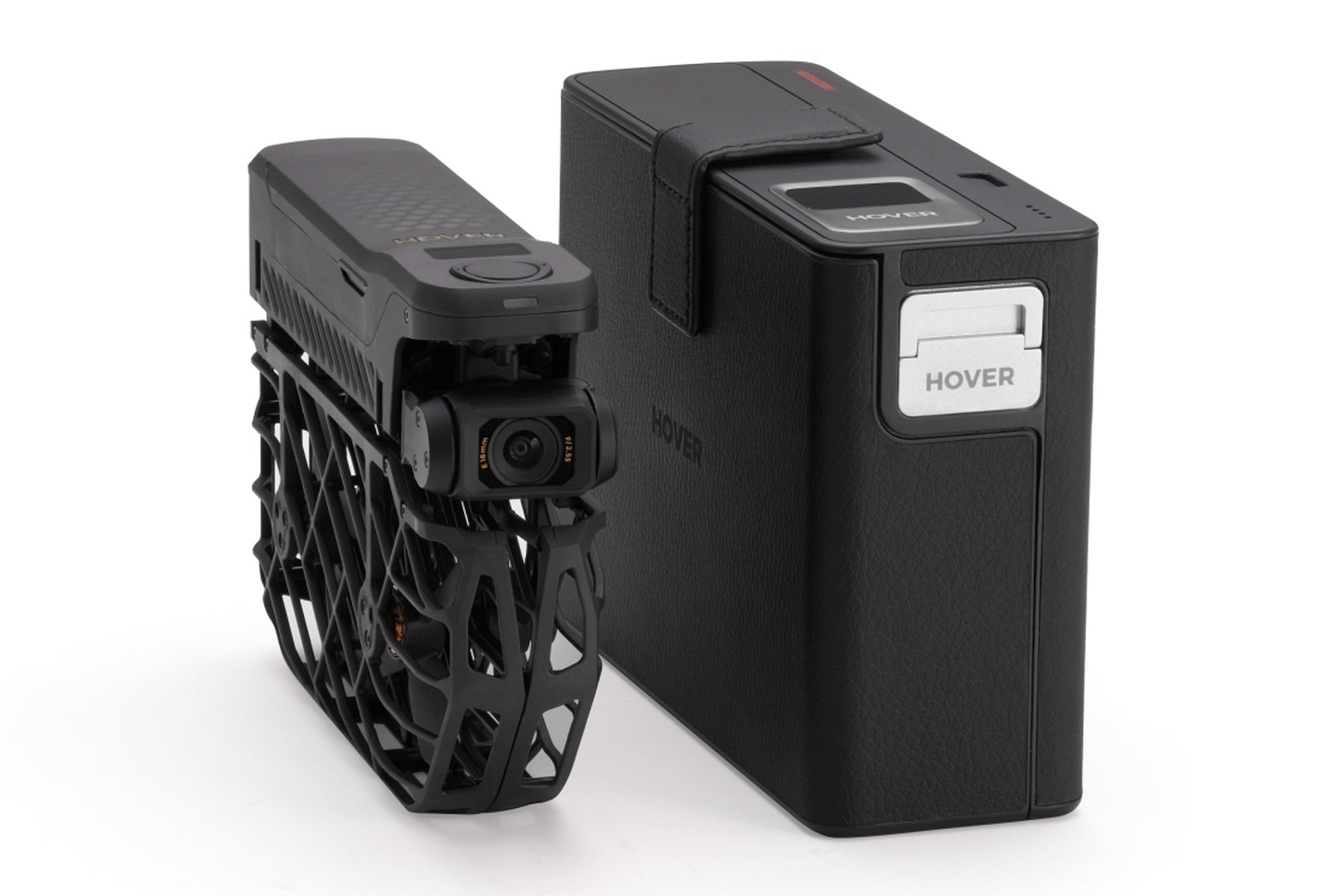 The compact black HOVERAir drone, featuring OmniTerrain capabilities and a protective frame, comes with a rectangular black storage case labeled "HOVERAir Power Case." It has an AI tracking system and transforms into an 8K flying action camera for capturing stunning footage from any angle.