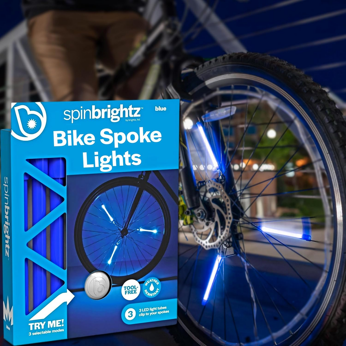 A bike with blue LED spoke lights zooms by, showcasing a weather-resistant design. The "Spin Brightz" packaging by Brightz is prominently displayed in the foreground, highlighting its vibrant features and branding.