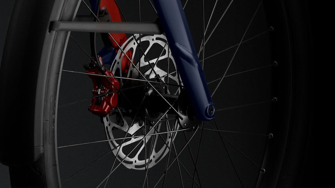 Close-up of a Stromer ST7 Alinghi Red Bull Racing Edition's front wheel, focusing on the disc brake and spokes with a blue and grey frame visible.