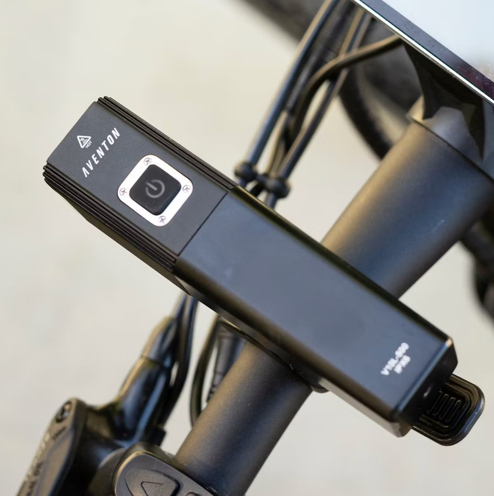 Close-up of a black USB rechargeable headlight mounted on the handlebar of a bicycle, with the brand name "Tampa Bay eBikes" visible on the light.