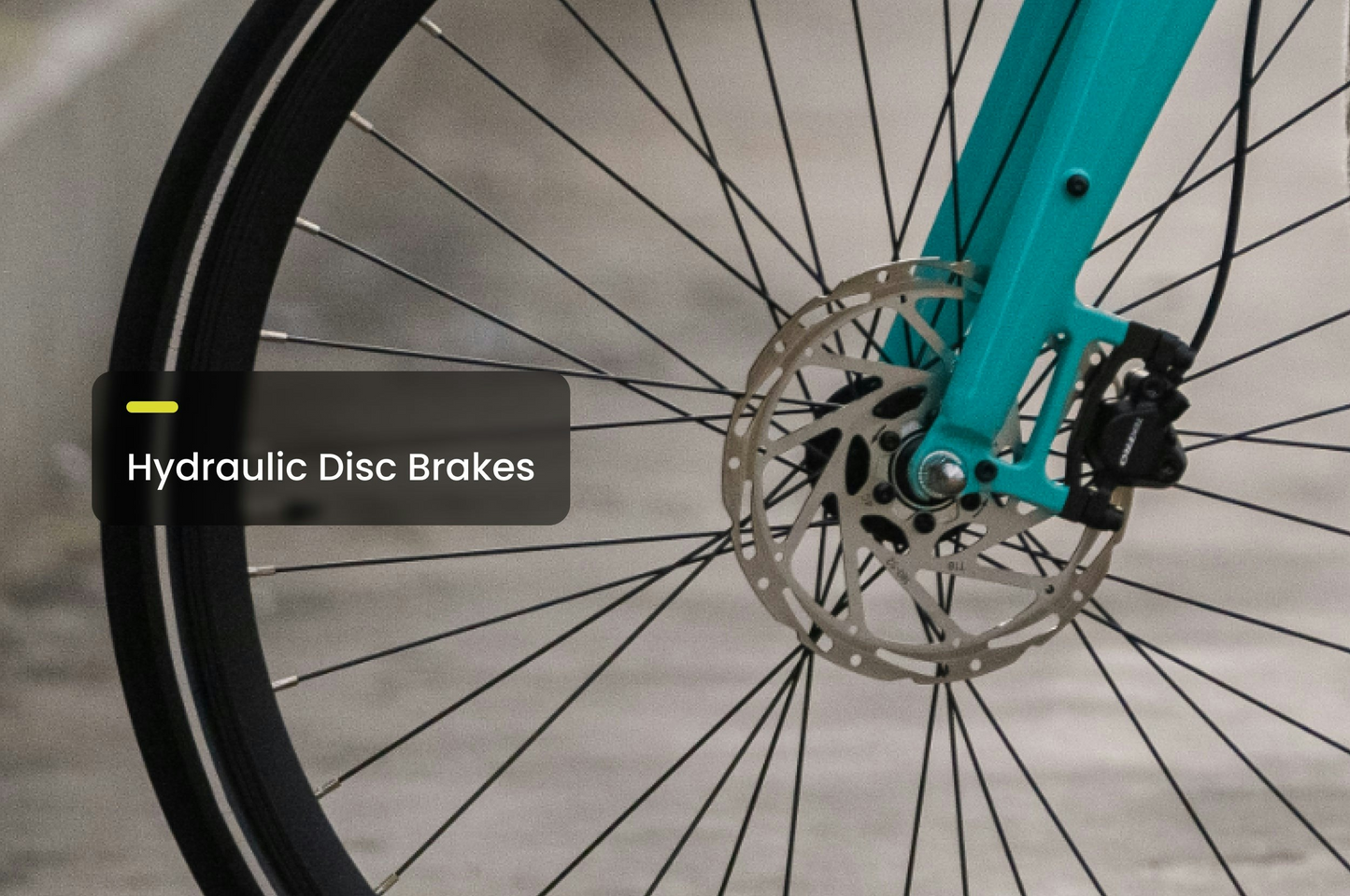 Close-up of an Aventon Soltera 2.5 bicycle front wheel, featuring hydraulic disc brakes, a torque sensor, and spokes, set against a blurred background.