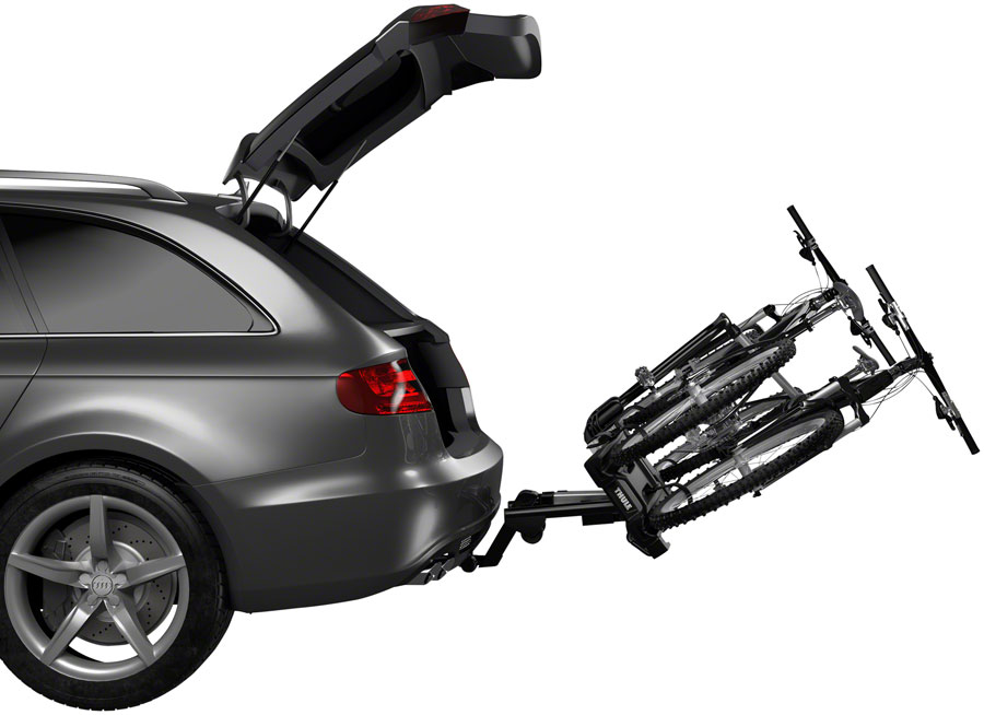 A silver car with its rear hatch open features a Thule EasyFold XT Hitch Bike Rack mounted at the back. Two e-bikes are securely fastened, highlighting the car's readiness for any adventure.