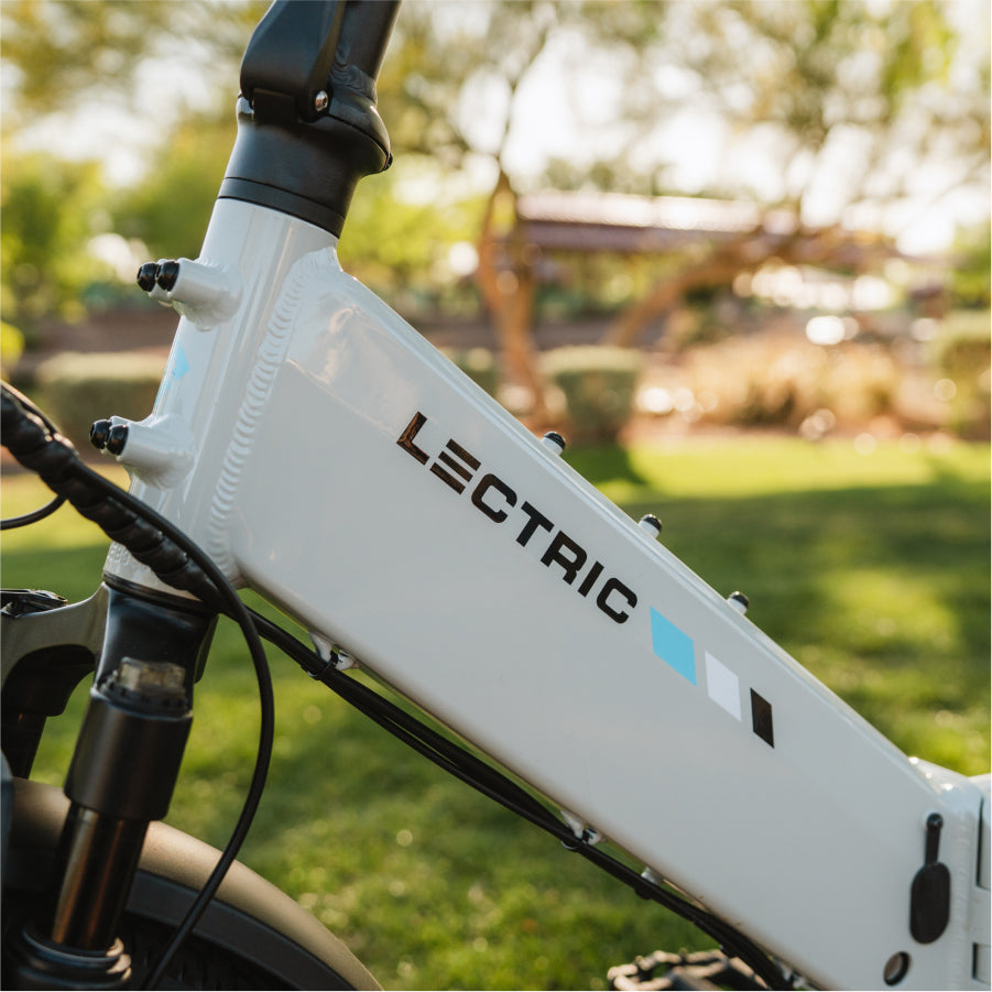 Close-up of a white Lectric - XP4 folding eBike frame with colorful design, featuring advanced Torque Sensor Technology, photographed outdoors against lush greenery.