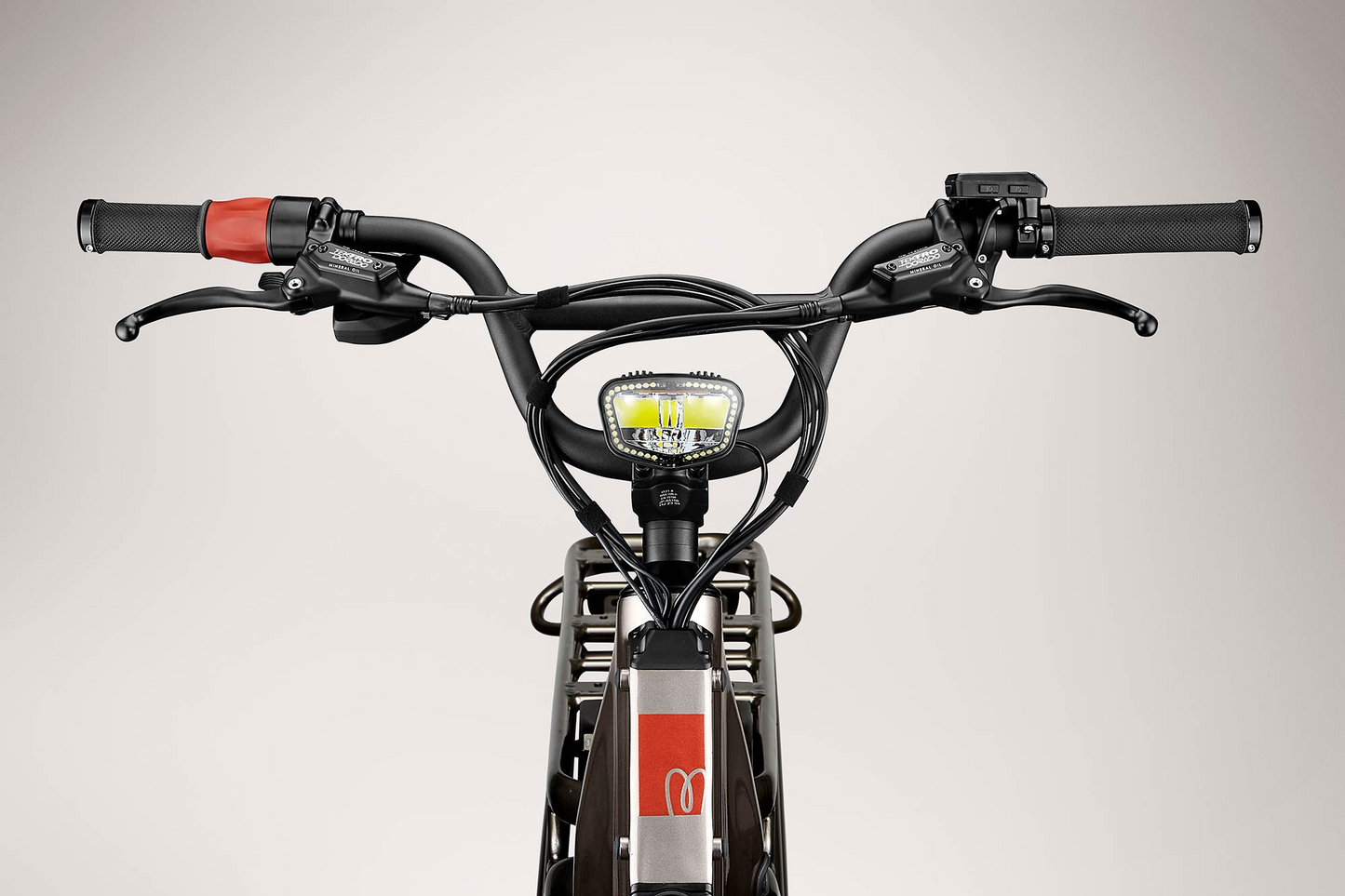 Close-up view of a Momentum - Cito E+ electric bicycle's handlebars with grips, brake levers, display screen, and front led light, against a gray background.