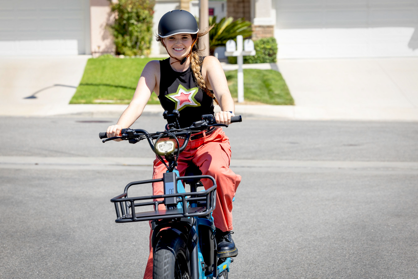 Young girl in a helmet smiling while riding a Momentum Cito E+ electric bike on a sunny suburban street.