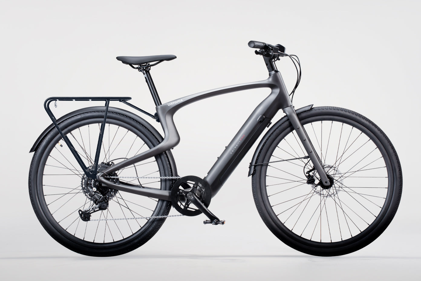 The Urtopia Carbon 1 Pro electric bicycle, in sleek gray with a modern lightweight aluminum frame, disc brakes, and a petite rear luggage rack, is elegantly displayed against a plain white background.