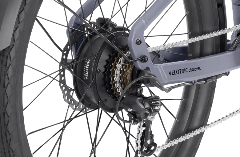 Close-up of the rear wheel and gears of a Velotric - Discover 1 Plus commuter e-bike, showcasing the drivetrain, chain, and derailleurs powered by the powerful Velopower H50 drive system.