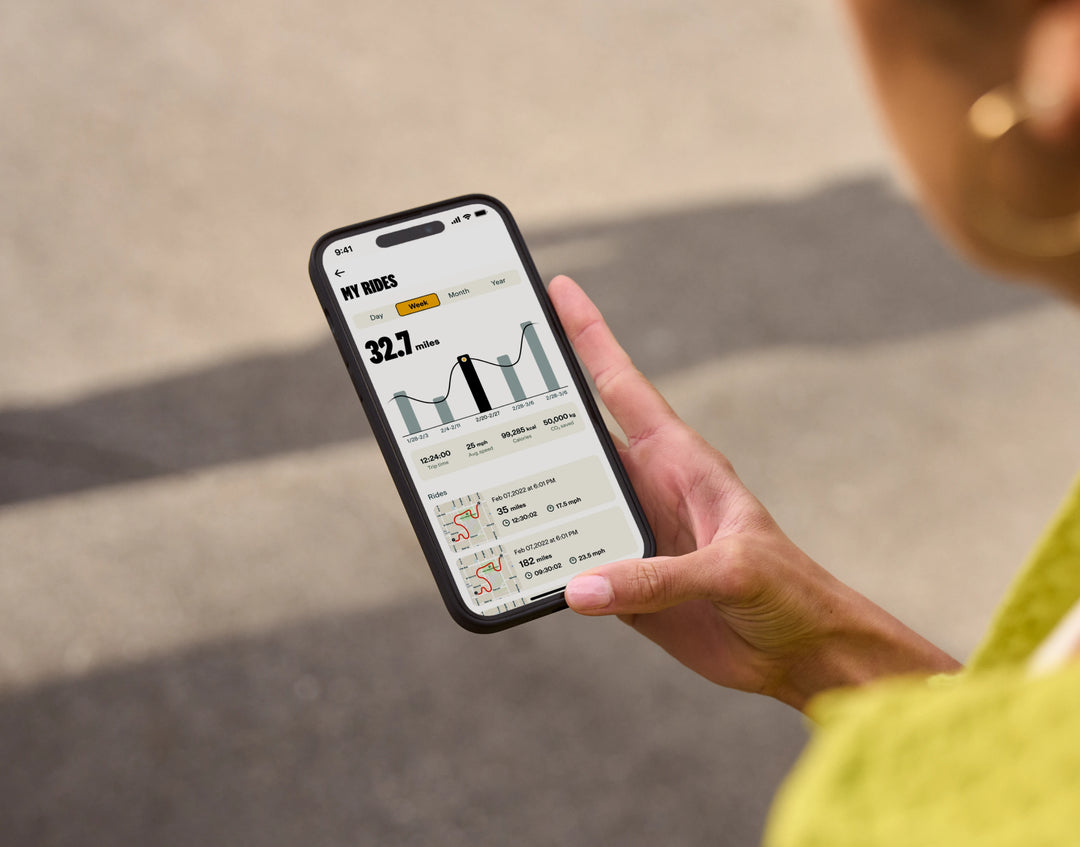 A person holds a smartphone displaying a cycling app with stats and charts of a cycling route. The screen shows distance, elevation, and a map, all perfectly suited for planning rides with the Velotric - Discover 1 Electric Bike.