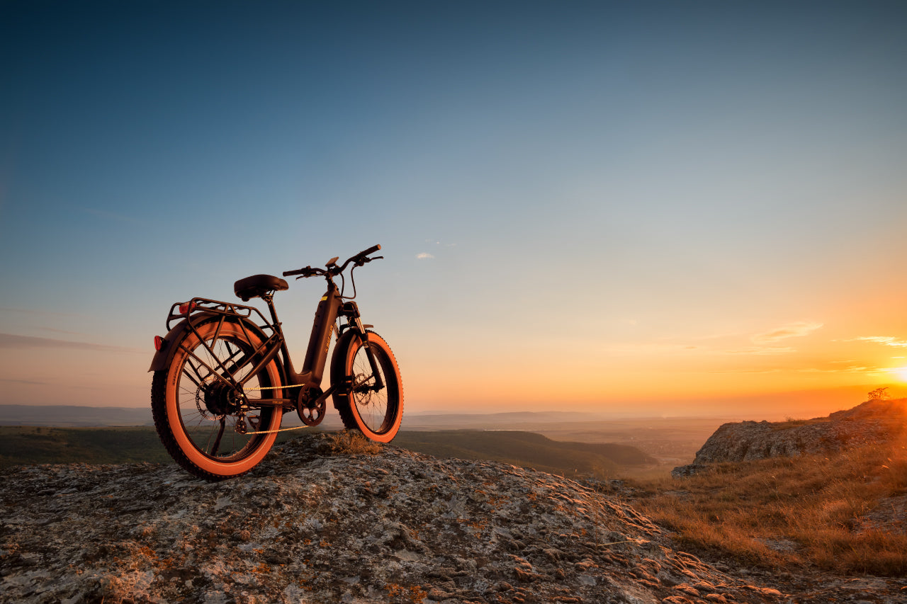 An all-terrain AIMA - Big Sur stands atop a rocky hill at sunset, its powerful motor ready to conquer the expansive landscape visible in the background.