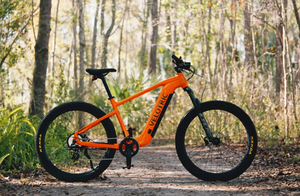 A Velotric Summit 1 eBike parked on a dirt path in a sunlit forest.