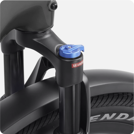 Close-up of a bicycle fork and suspension system with a blue adjuster knob marked "LC-LOCK." The tire beneath is labeled "LEND." This setup is featured on the Velotric Discover 1, an impressive electric bike built for smooth rides.