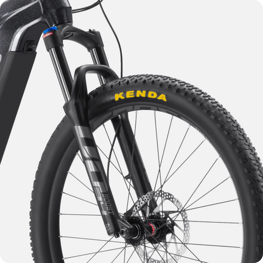 Close-up of a Velotric Summit 1 eBike front wheel with detailed view of the suspension fork and Kenda tire, showcasing the disc brake and cleanly routed cables.